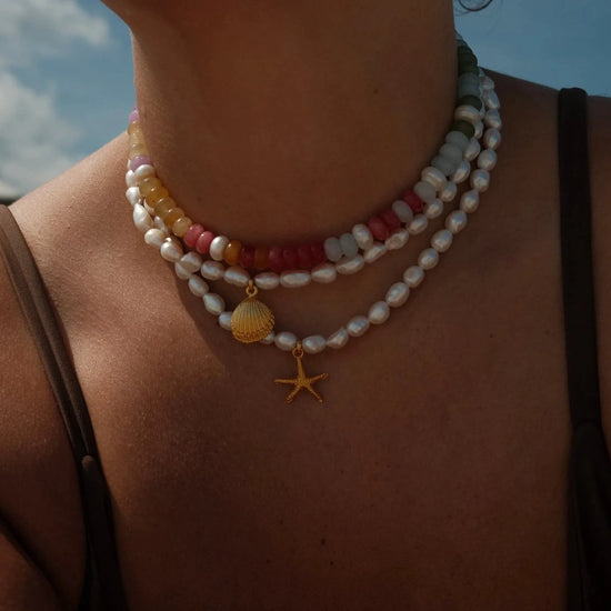 Close-up of a person wearing a necklace with starfish charm against a blurred outdoor background