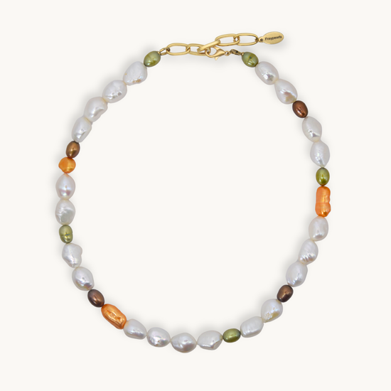 A necklace featuring baroque white, small olive green, brown, and orange pearls, accented with a gold chain clasp, shown on a light cream background.