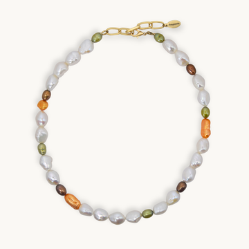 A necklace featuring baroque white, small olive green, brown, and orange pearls, accented with a gold chain clasp, shown on a light cream background.