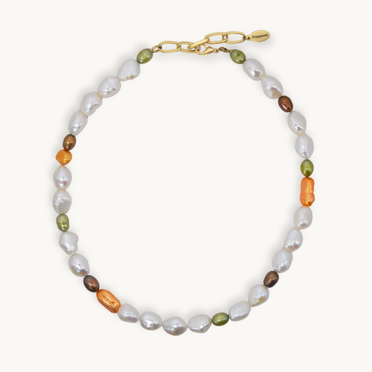 A necklace featuring baroque white, small olive green, brown, and orange pearls, accented with a gold chain clasp, shown on a light cream background.