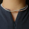 A close-up image of a neck wearing two elegantly intertwined pearl necklaces in shades of white and pink. The person is dressed in a textured dark top.