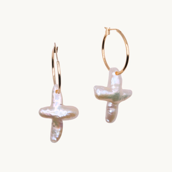 Gold hoop earrings with irregularly shaped cross-like pearl pendants on a light background. The design conveys a modern, elegant style.