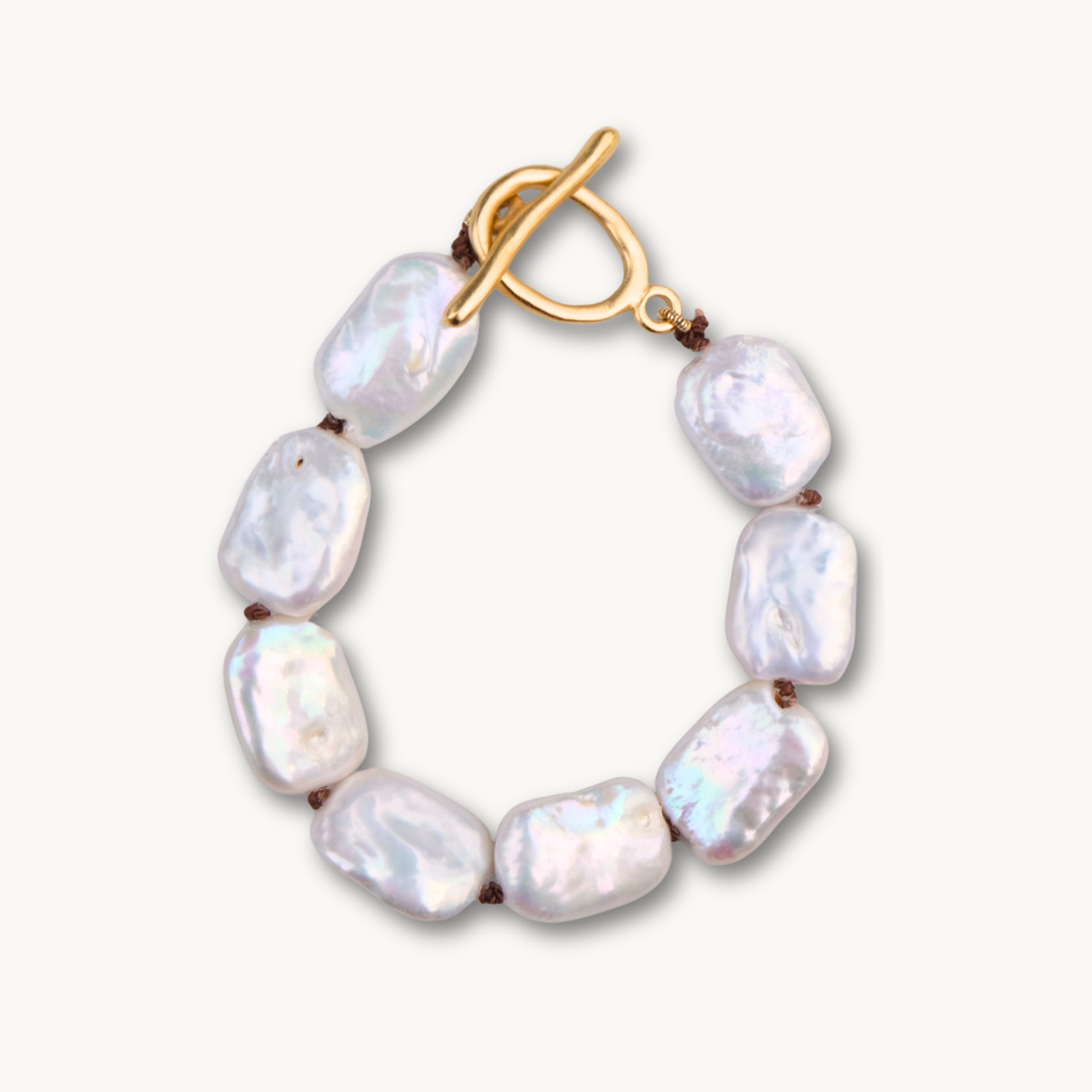 A stylish bracelet with seven white baroque pearls connected by brown knots and a gold toggle clasp. The pearls have an iridescent sheen on a pale background.
