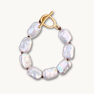 A stylish bracelet with seven white baroque pearls connected by brown knots and a gold toggle clasp. The pearls have an iridescent sheen on a pale background.