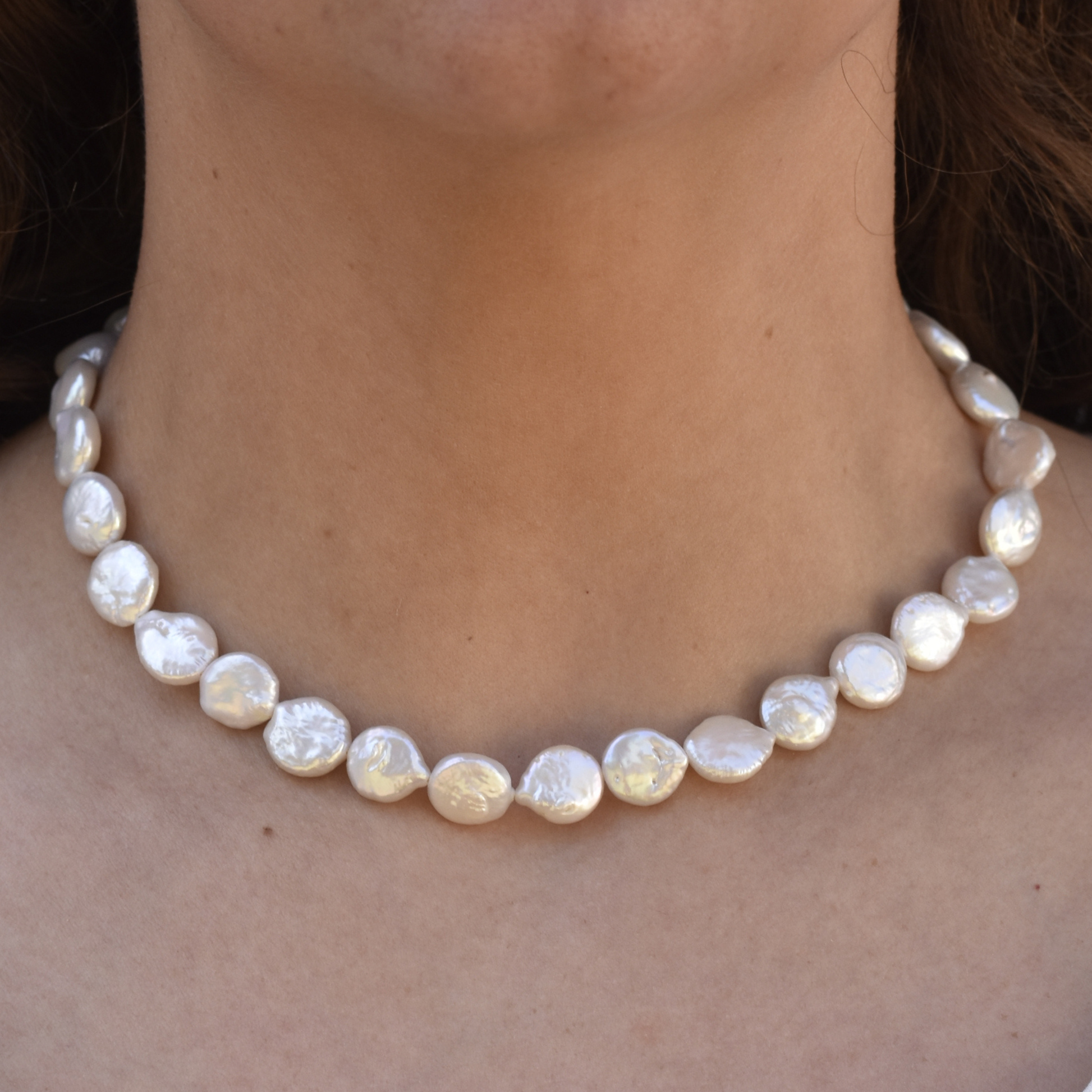 A close-up of a woman's neck wearing a necklace of round, white, shiny pearls. The elegant pearls reflect light, creating a classic, sophisticated look.
