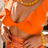 Woman in orange set wearing chunky pearl and yellow necklace and bracelet