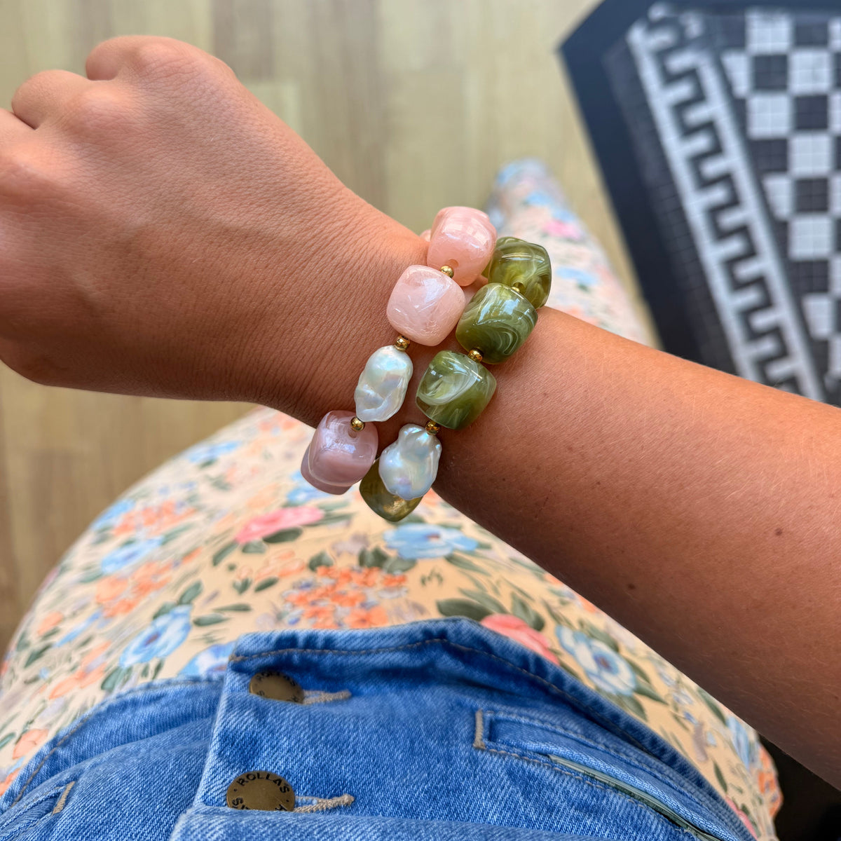 A close-up of a person's wrist wearing three beaded stretch bracelets. The bracelets feature irregular baroque-style beads in pink, olive green, and milky white, with gold-toned metal spacers.