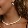 Close-up of a woman wearing a pearl beaded necklace and matching heart-shaped pearl drop earring with gold-tone hoops.