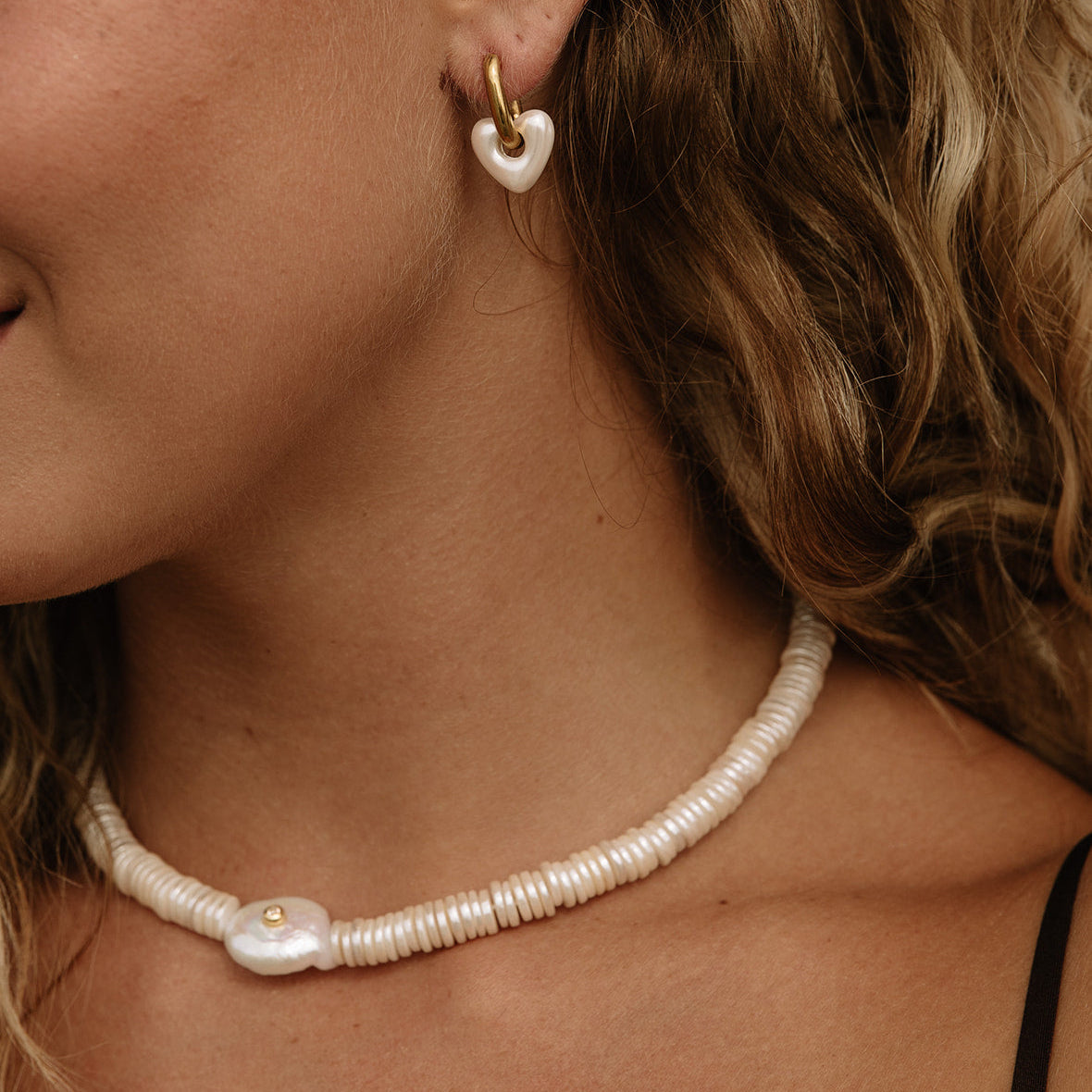 Close-up of a woman wearing a pearl beaded necklace and matching heart-shaped pearl drop earring with gold-tone hoops.