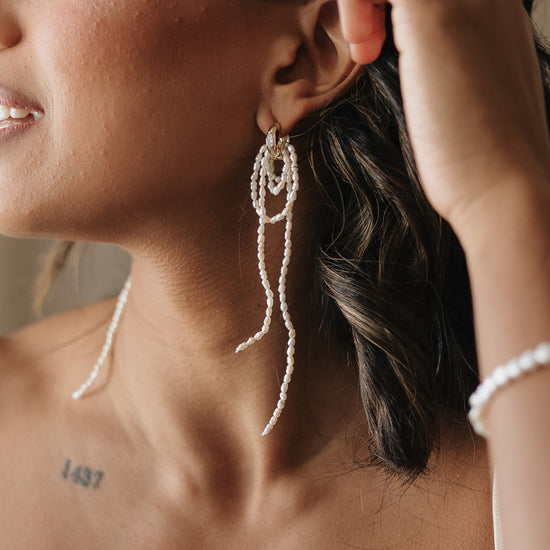 Close-up of a person wearing pearl drop earrings with a blurred background for brides and wedding guests. 