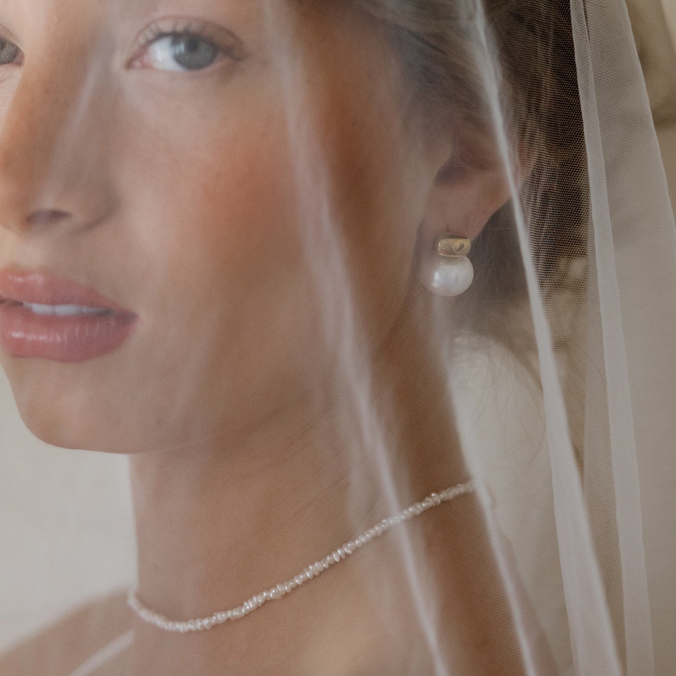 Close-up of a bride wearing pearl earrings and a necklace with a veil.