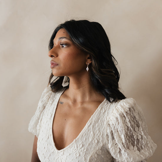Bride wearing bridal gown with soft curls showcasing her timeless pearl and diamond pairing earrings. 
