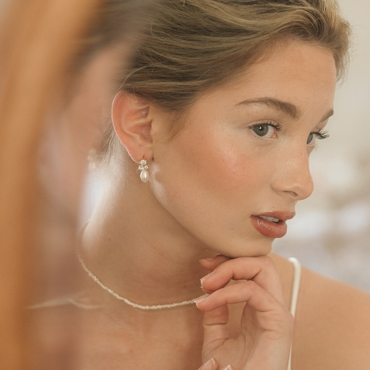 Bride with a bun hairstyle wearing a delicate pearl necklace, with classic diamond and pearl earrings