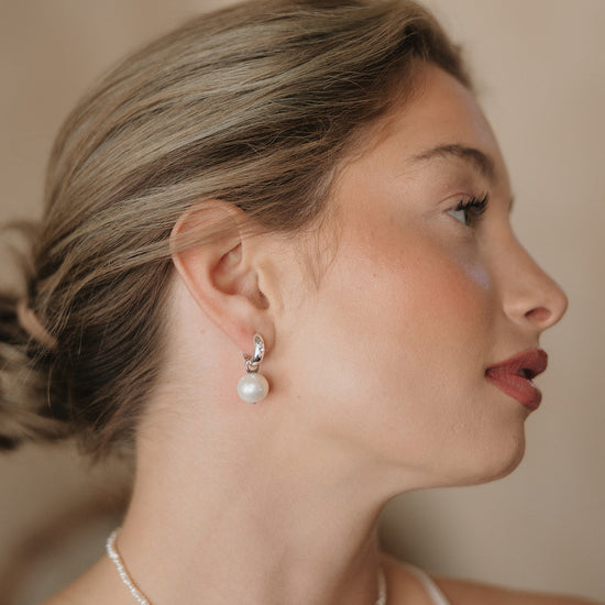 Woman wearing pearl earrings and a necklace against a neutral background