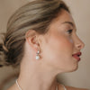 Woman wearing pearl earrings and a necklace against a neutral background