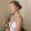 Woman wearing a white dress with thin straps against a beige background. She is adorned with abstract shaped bridal pearl jewelry. 