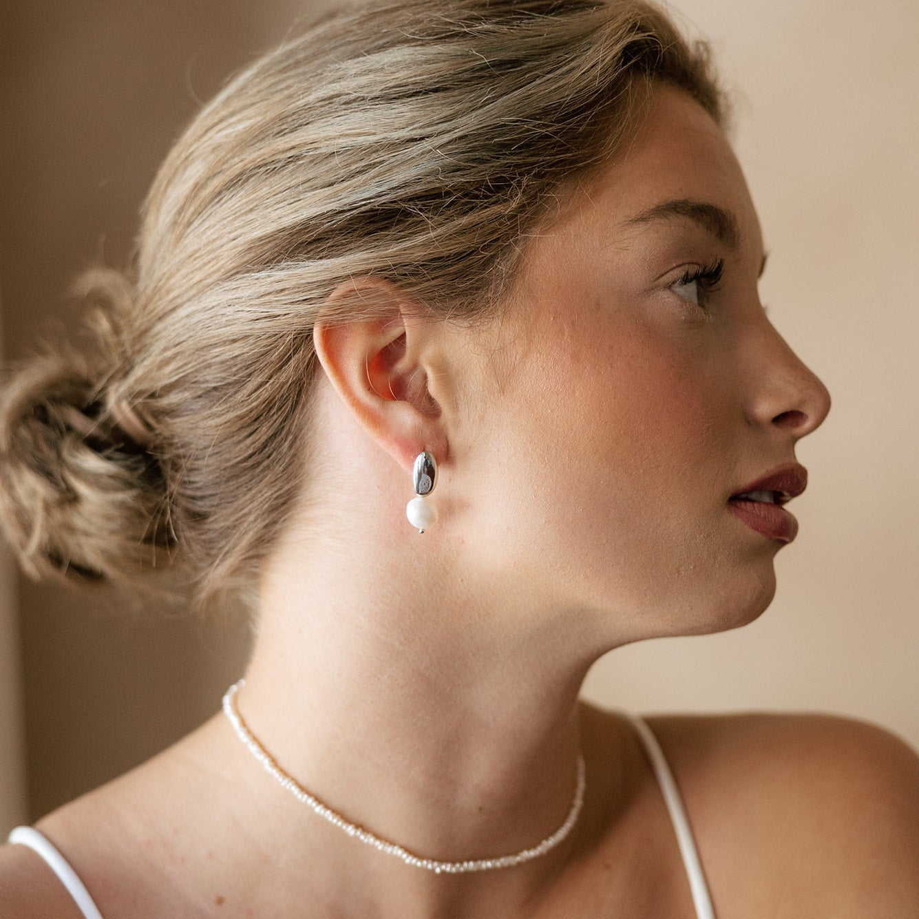 Bride wearing pearl earrings and a delicate pearl necklace with a neutral background