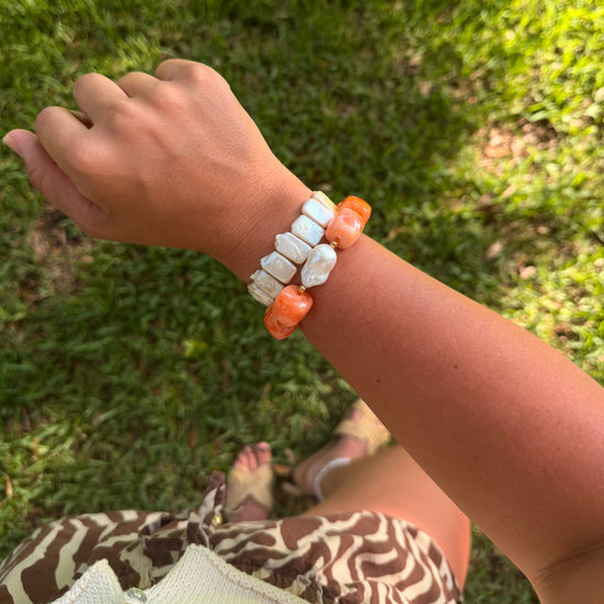 A person outdoors on grass wearing a beaded bracelet with white irregular stones and orange round accent beads.