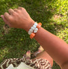A person outdoors on grass wearing a beaded bracelet with white irregular stones and orange round accent beads.