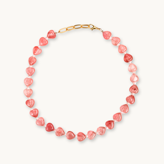 A necklace with translucent pink heart-shaped beads connected by small pearls, featuring a gold clasp, arranged in a semicircle on a white background.