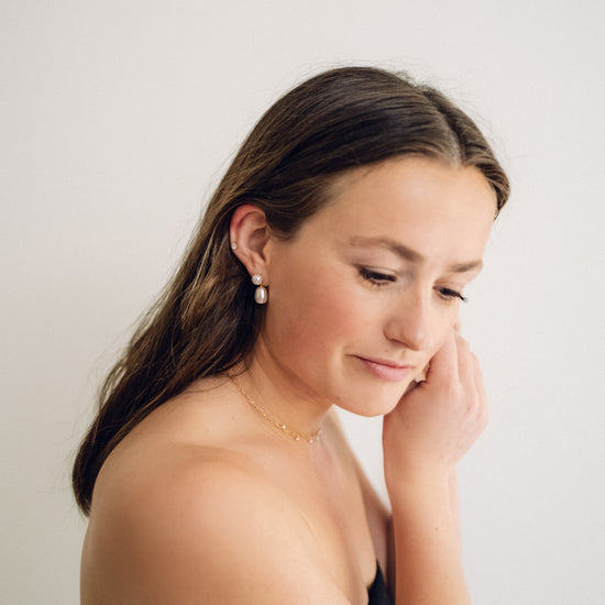 Woman with long brown hair wearing a black top against a plain background