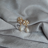 Elegant pearl earrings on a textured silver fabric. The earrings feature gold floral settings with teardrop pearls, conveying sophistication and luxury.