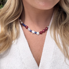 A woman wears a red, white, and blue star-pearl necklace over a cream knit sweater. Her blond hair is partially visible, and the tone is casual and elegant.