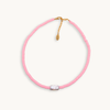 A vibrant pink bead necklace featuring a single, irregularly-shaped gray pearl at the front. Gold clasp and chain links add a touch of elegance.