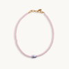 A soft pink bead necklace featuring a single, irregularly-shaped gray pearl at the front. Gold clasp and chain links add a touch of elegance.