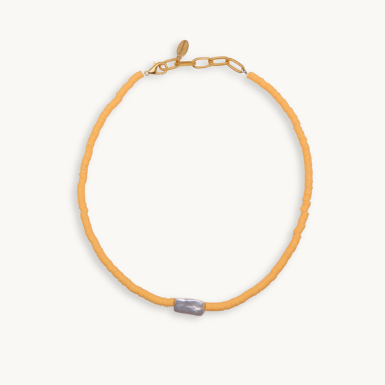 A vibrant orange bead necklace featuring a single, irregularly-shaped gray pearl at the front. Gold clasp and chain links add a touch of elegance.