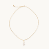 Gold necklace with a small pearl cross pendant on a white background