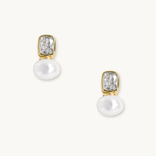 Elegant earrings with rectangular clear gemstones in gold settings and attached white pearls, set against a light background. Luxurious and refined.