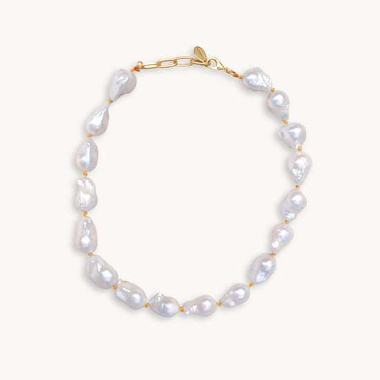 A baroque pearl necklace with irregular white pearls strung along a delicate yellow string. The lustrous pearls convey an elegant, natural look.