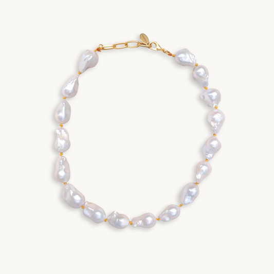 A baroque pearl necklace with irregular white pearls strung along a delicate yellow string. The lustrous pearls convey an elegant, natural look.