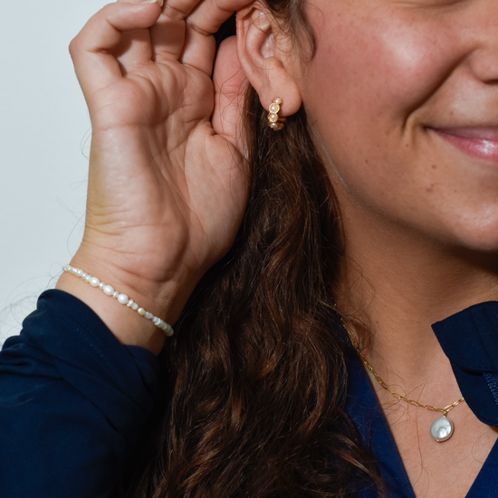 Close-up of a woman smiling, wearing pearl earrings, necklace, and bracelet. Her hand is touching her ear, showing joy and elegance.