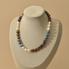A multi-colored baroque pearl necklace displayed on a beige fabric jewelry bust against a solid beige background.