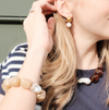 Woman's profile with blond hair wearing a striped top, showcasing a pearl earring, chunky bracelet, brown bead and pearl necklace. Mood is stylish and elegant.