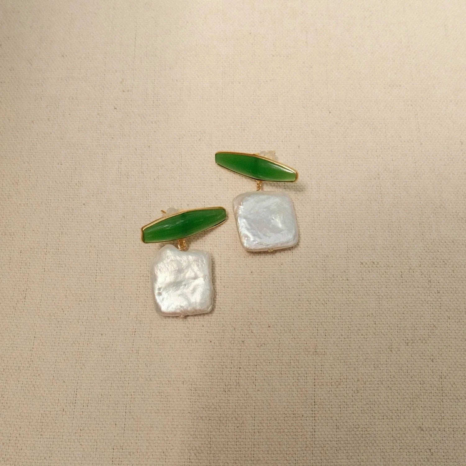 Green stone and iridescent pearl earrings on a beige fabric. Earrings contrast with delicate peach, blue, and lavender flowers on beige.