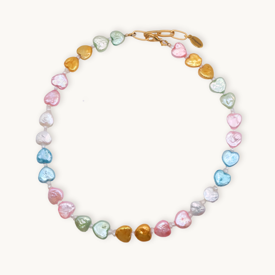 A colorful necklace featuring heart-shaped beads in pink, blue, gold, green, and white hues with a gold clasp, conveying a playful and vibrant tone.