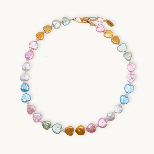 A colorful necklace featuring heart-shaped beads in pink, blue, gold, green, and white hues with a gold clasp, conveying a playful and vibrant tone.
