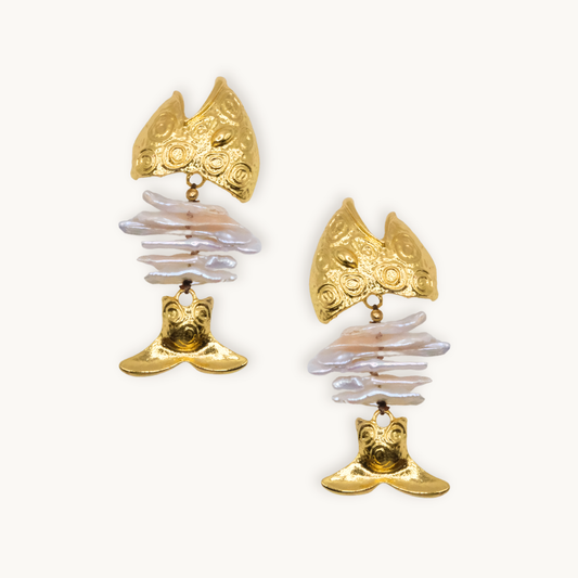 Gold earrings with a textured fish design feature layered white pearls as the body. The overall look is both artistic and elegant, conveying luxury.