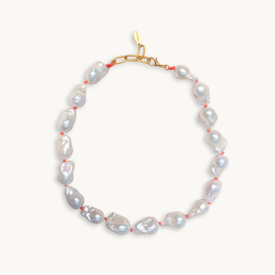 A baroque pearl necklace with irregular white pearls strung along a delicate red string. The lustrous pearls convey an elegant, natural look.