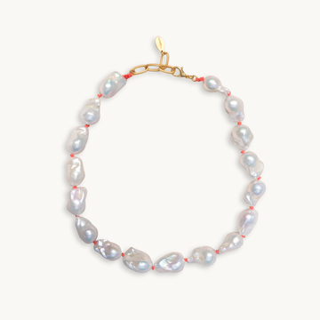 A baroque pearl necklace with irregular white pearls strung along a delicate red string. The lustrous pearls convey an elegant, natural look.