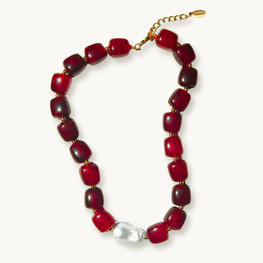 Red beaded necklace with chunky, glossy beads and a gold clasp and baroque pearl, exuding an elegant and bold style. Gold accents add a touch of sophistication.