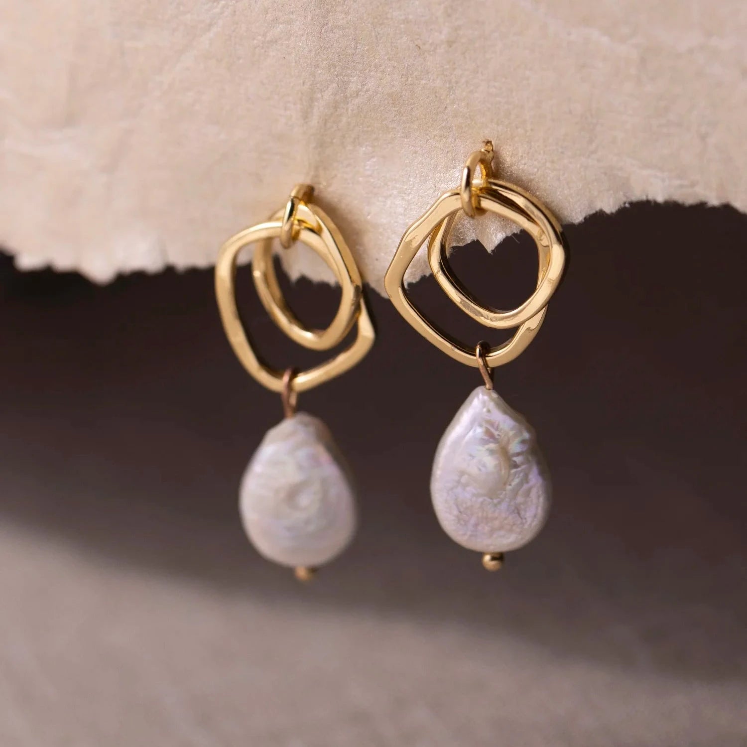 Elegant gold earrings with abstract loop design and tear-shaped pearl drops, set against a neutral background, conveying a classy tone.