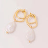Gold earrings with intertwined geometric loops and dangling baroque pearl drops on a light background, conveying elegance and sophistication.