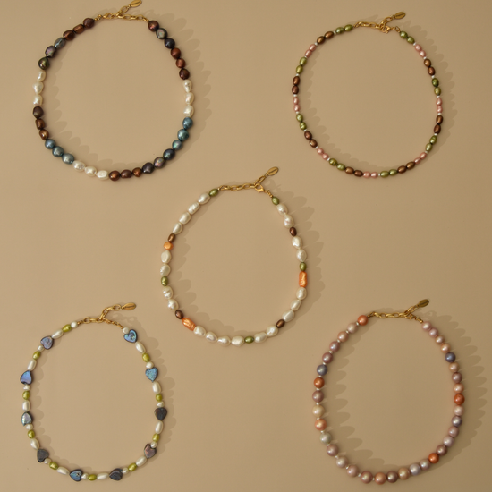 Five beaded baroque pearl necklaces with gold clasp closures, displayed in a flat-lay arrangement on a solid beige background.