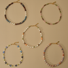 Five beaded baroque pearl necklaces with gold clasp closures, displayed in a flat-lay arrangement on a solid beige background.
