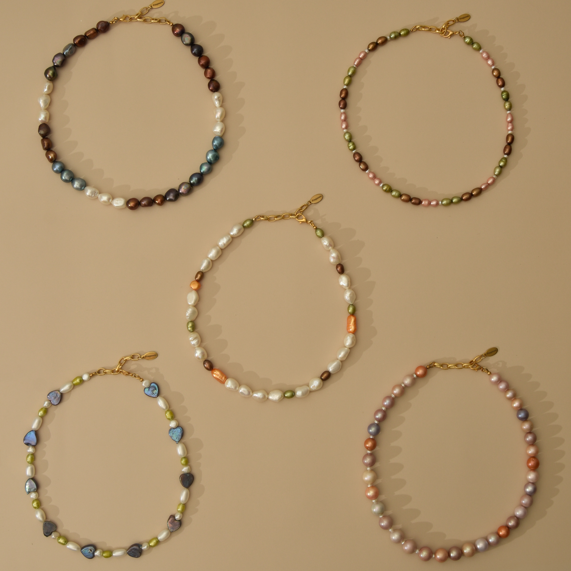 Five beaded baroque pearl necklaces with gold clasp closures, displayed in a flat-lay arrangement on a solid beige background.