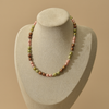 A multi-colored freshwater pearl necklace displayed on a textured beige jewelry bust against a solid warm beige background.